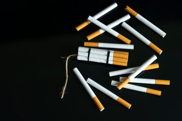 Cigarettes, in the form of sticks of dynamite, lie among the scattered cigarettes on a black reflective surface.