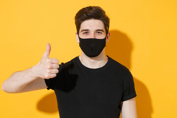 Young guy in casual black t-shirt face mask isolated on yellow background studio portrait. Epidemic...