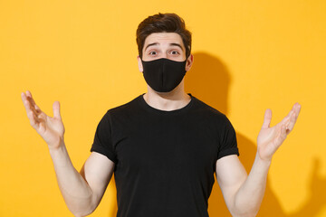 Shocked young man guy in black t-shirt face mask isolated on yellow wall background studio...
