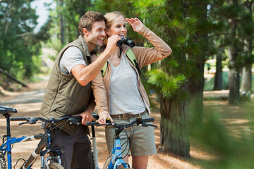 Smiling couple with mountain bikes using binoculars in woods