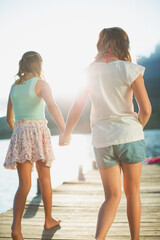 Sisters holding hands on dock over lake