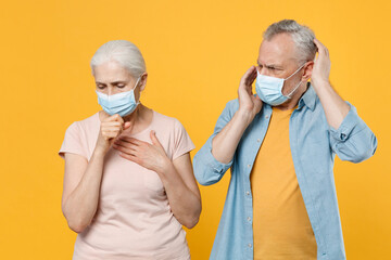 Elderly gray-haired couple woman man in sterile face mask isolated on yellow background studio....