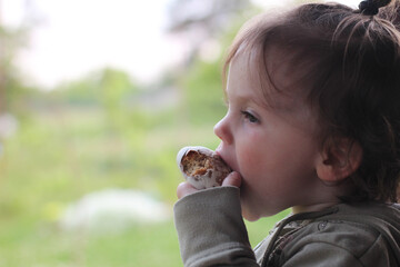 Little beautiful baby in profile gnawing a bun on blurred natural background