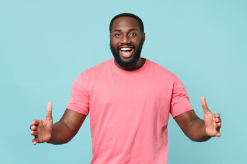 Fototapeta premium Excited young african american man guy in casual pink t-shirt isolated on blue background studio. People lifestyle concept. Mock up copy space. Gesturing demonstrating size with horizontal workspace.