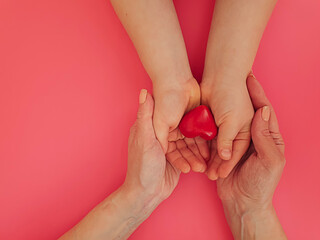 hands of mom and baby hold a heart on a colored background
