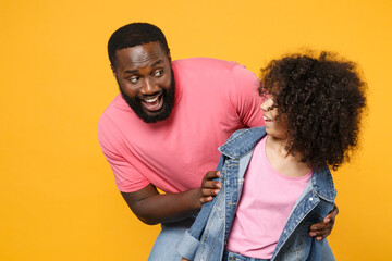 Fototapeta premium Excited african american guy girl brother sister in denim pink clothes posing isolated on yellow wall background studio portrait. People lifestyle concept. Mock up copy space. Looking at each other.