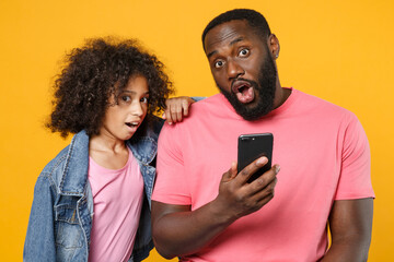 Shocked african american guy girl brother sister in denim pink clothes posing isolated on yellow background studio. People lifestyle concept. Mock up copy space. Using mobile phone typing sms message.