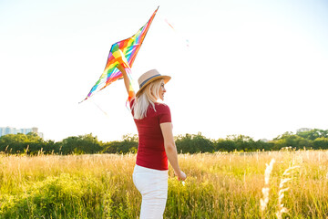 Beauty girl running with kite on the field. Beautiful young woman with flying colorful kite over clear blue sky. Free, freedom concept. Emotions, healthy lifestyle