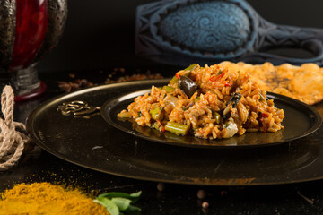 Pilaf with vegetables in a plate on a black wooden table