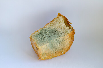 Half a loaf of white bread with blue and green mold on a white background. Selective focus. Moldy, spoiled bread.