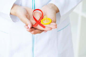 Doctor holding a red ribbon and condom calling for safe sex and protection from AIDS