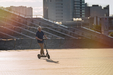 Senior man riding electric kick scooter in the cityscape at sunset    