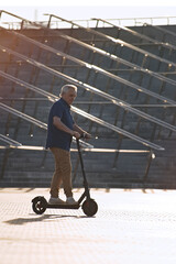 Senior man riding electric kick scooter in the cityscape at sunset    