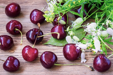 Big sweet juicy cherries, foliage and flowers on wooden background, top view, concept of a healthy diet, harvest, natural food.