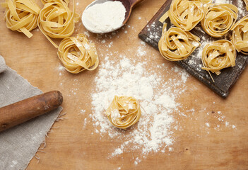 raw fettuccine pasta on a brown wooden board and a wooden vintage rolling pin