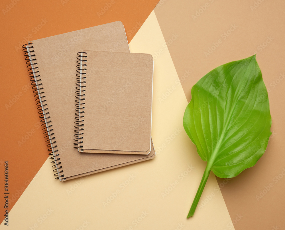 Poster stack of spiral open notebooks with blank brown sheets on a beige background
