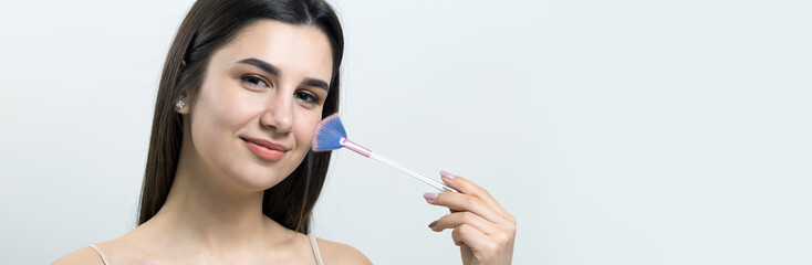 Close-up of a young girl in a light top on a white background making a facial make-up. A pretty...