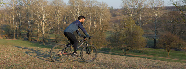 Naklejka na ściany i meble Cyclist in shorts and jersey on a modern carbon hardtail bike with an air suspension fork standing on a cliff against the background of fresh green spring forest