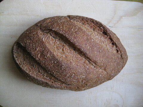 pan de levadura madre, hogaza de forma oval con tres grietas de cocci&oacute;n sobre tabla madera.
