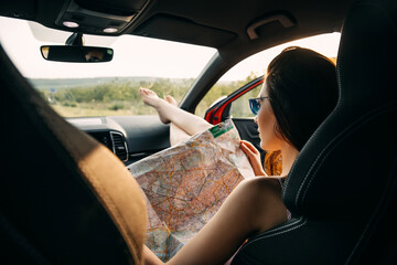 Young woman sitting in car, looking to a map, planning new trip. City break concept.