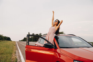 Young beautiful woman with hands up in the air, enjoying summer wind next to her car. Summer vacation concept.