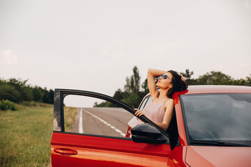 Young beautiful woman relaxing and enjoying summer wind next to her car. Summer city break concept.