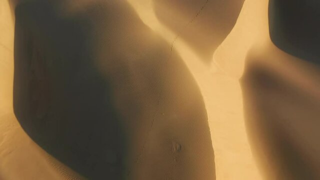 4K top down view on the abstract wavy pattern on the sand desert surface painted by the sunset light and deep shadows on the high dunes. Beautiful aerial background of the wild nature scenic landscape