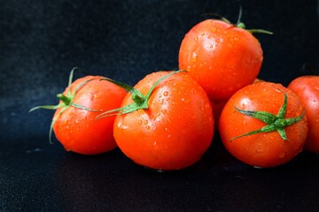 Red ripe juicy tomato with a green stalk with drops of water on a black background close-up.