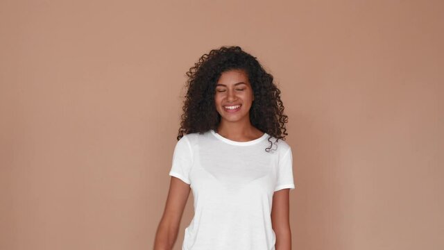 black woman smiling laughing and waving hello to camera isolated on brown