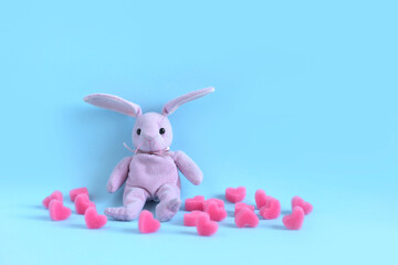 Obraz premium Pink plush hare sits on blue background among soft pink hearts. Valentine's day card