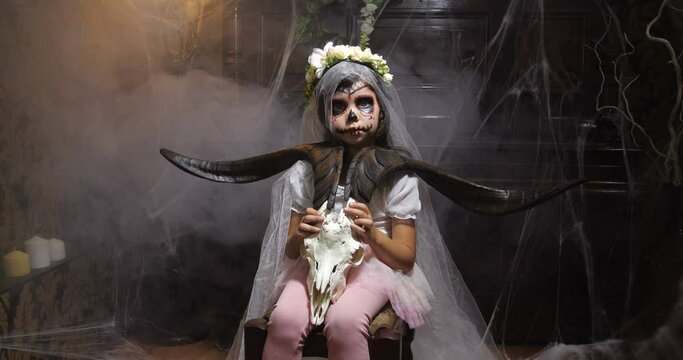 Portrait of girl dressed in Halloween Santa muerte costume  holding a goat scull in of old dark Gothic interior covered with cobwebs and mysterious fog and  changing lighting. 4K slow motion 50 fps