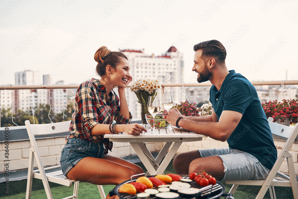 Sticker Young couple in casual clothing enjoying romantic dinner and smiling while enjoying romantic dinner on the rooftop patio outdoors