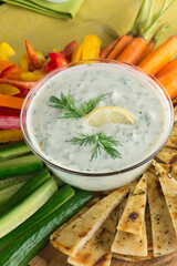 Tzatziki. Traditional Greek or Turkish homemade dip. Made with Greek yogurt, cucumbers, lemon juice, olive oil and dill. Served with mini rainbow carrots & crispy pita chips on a wooden cutting board