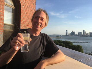 Caucasian man having a gin and tonic on a rooftop bar in Manhattan, late summer afternoon. White man having a drink on a rooftop smiling, looking at camera.