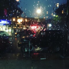 Looking out rain spattered window of a bar onto the commercial businesses and busy street in Queens, New York. Night light shining through window covered in rain drop during heavy rain storm, filtered