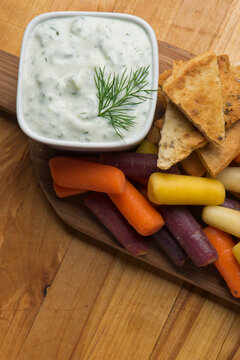 Tzatziki. Traditional Greek Or Turkish Homemade Dip. Made With Greek Yogurt, Cucumbers, Lemon Juice, Olive Oil And Dill. Served With Mini Rainbow Carrots & Crispy Pita Chips On A Wooden Cutting Board