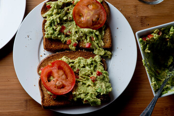 Avocado Toast. Classic American Diner Breakfast or Brunch Restaurant menu item: avocado toast. Made w/ fresh avocados smashed into guacamole and chopped tomatoes with salt and pepper served on toast.