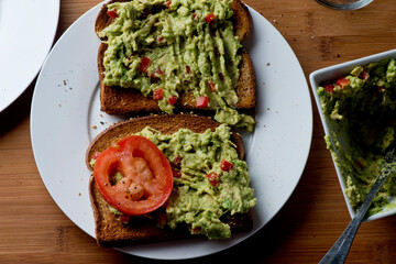 Avocado Toast. Classic American Diner Breakfast or Brunch Restaurant menu item: avocado toast. Made w/ fresh avocados smashed into guacamole and chopped tomatoes with salt and pepper served on toast.