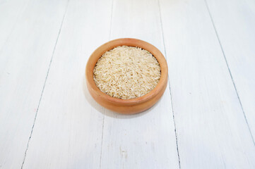 A bowl filled with uncooked brown rice. On top of a white wood table