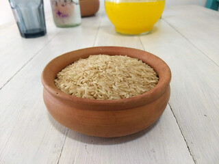 A bowl filled with uncooked brown rice. On top of a white wood table