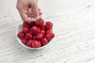 The male hand takes strawberries from a white plate, in which lies a lot of strawberries, against a...