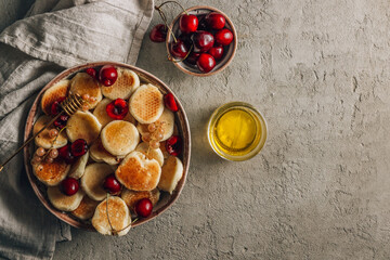 Fototapeta na wymiar Trendy home breakfast with tiny pancakes, honey and cherries on a concrete table.