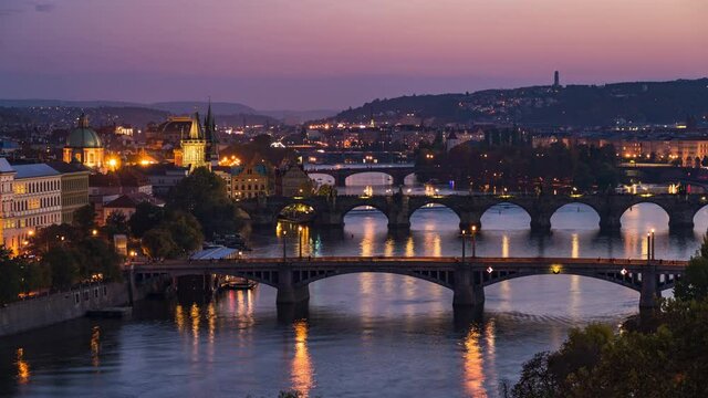 Prague, Czech Republic, zoom out timelapse view of Prague cityscape showing medieval bridges and boats on Vltava river at dusk.