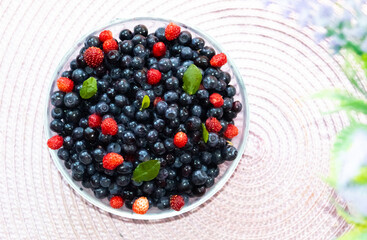 Fresh bilberries and strawberries found in forest. Bright berries. Crop of bilberries and wild strawberries with green leaves. Red berries lay on blue berries