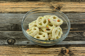 Pretzels dipped in white chocolate with sprinkles in glass bowl on table