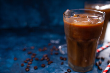 Cold cool summer drink, coffee with ice and milk on a background of a blue wall with coffee grains