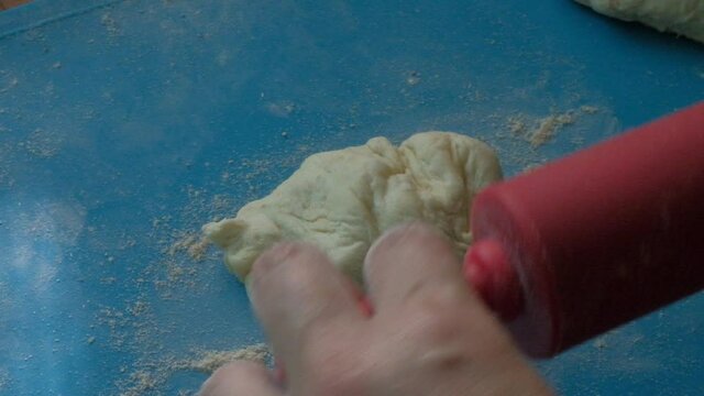 A gerl separates a small piece of dough and then rolls out the dough for pies with a small red rolling pin.