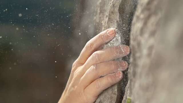 SLOW MOTION, MACRO, DOF: White magnesium powder flies in the air as rock climber scales a cliff and places her fingers into a small crack. Woman grabs an edge hold while scaling a challenging cliff.