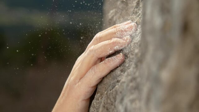 SLOW MOTION, MACRO, DOF: Unrecognizable rock climber with chalked up hands grips a sloper hold. Experienced female climber grips a sloper hold while scaling a dangerous cliff. Strong woman bouldering.