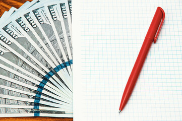 Close-up of US dollars spread out, an empty business notebook and pen